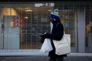 米ニューヨークでシャッターが閉まる店舗前を歩く人