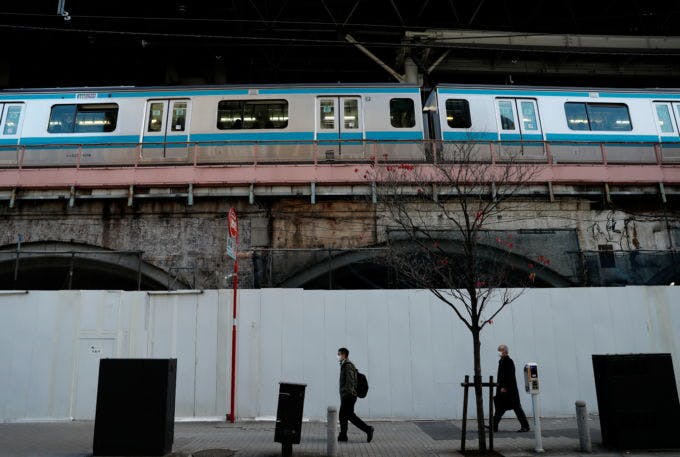 都内の駅に停まっている電車と線路沿いを歩く人