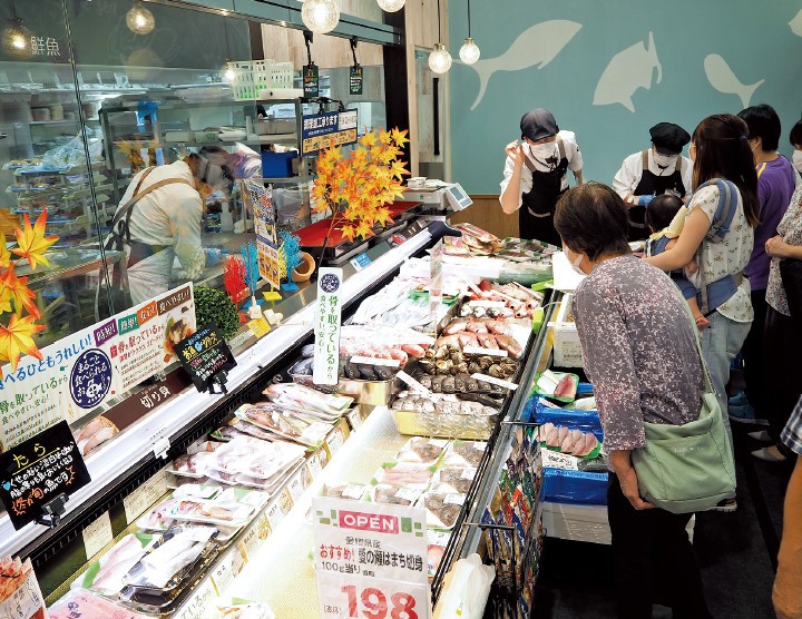 買い物客でにぎわうスーパーと接客をする従業員