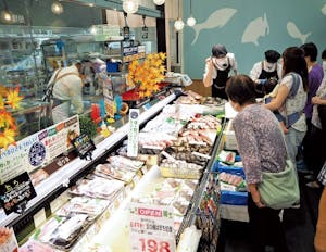 買い物客でにぎわうスーパーと接客をする従業員