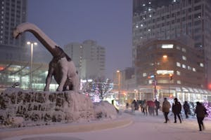 雪が降るＪＲ福井駅前にそびえ立つ恐竜モニュメントと帰宅する人たち
