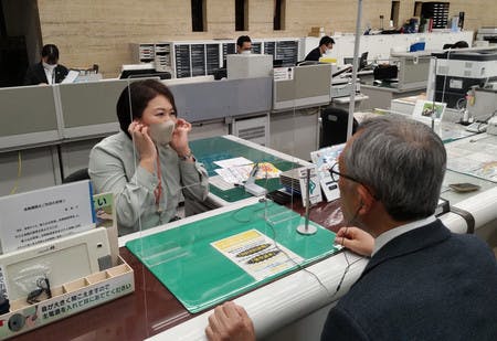 城南信用金庫の本店窓口で軟骨伝導の技術を用いたイヤホンを利用する客