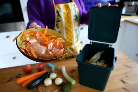 フランス・グラースで、堆肥にするためコンポスト容器に野菜くずを入れる女性