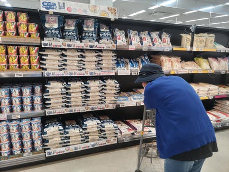 スーパーでコメの陳列棚を眺める客